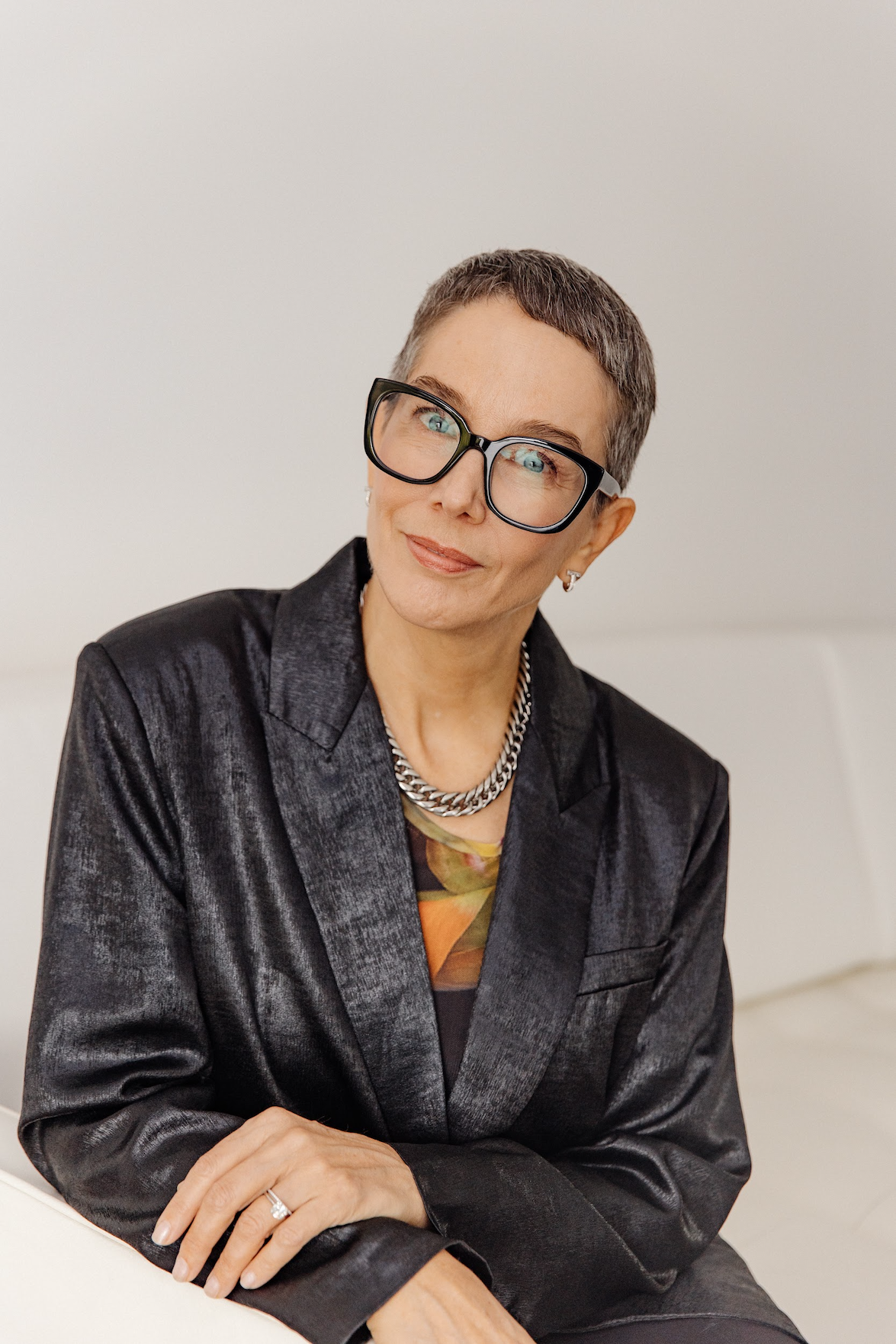 Seated woman with glasses and shiny black blazer
